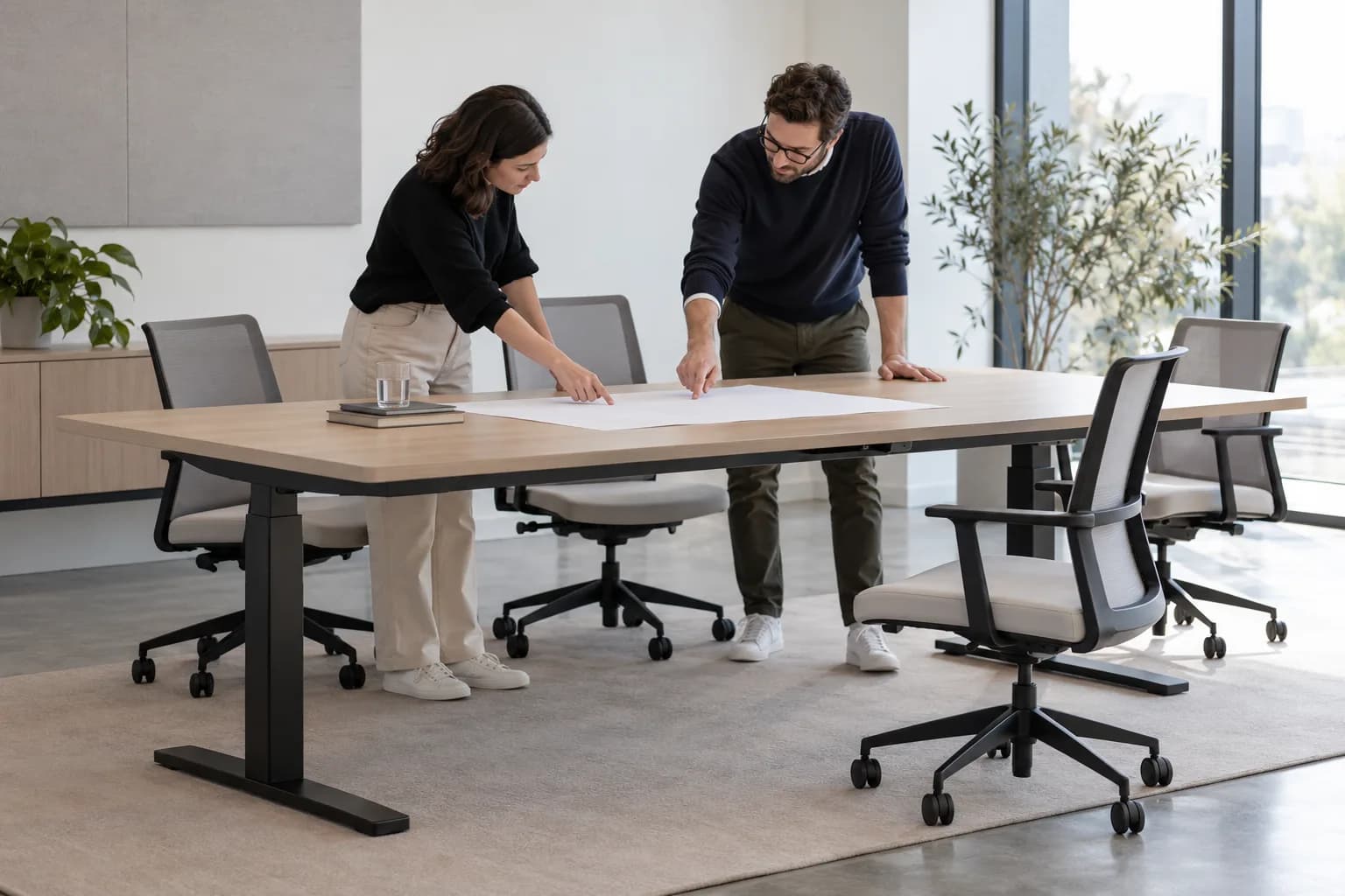Two planners reviewing a blank layout beside an illustrative adjustable conference table and office chairs